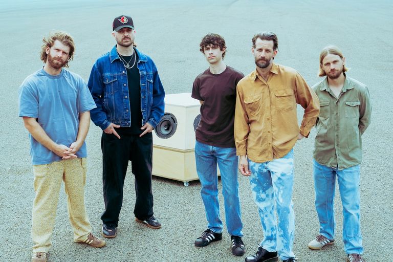 Australian alt-rock band The Rubens stand together on open pavement in casual streetwear around a custom wooden speaker box.